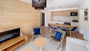 Ein modernes Wohnzimmer mit Fernseher, Sitzgelegenheiten, einem Couchtisch und einer Küche im Hintergrund.
