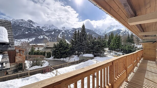 Ein Holzbalkon mit Blick auf verschneite Berge und einen klaren Himmel.
