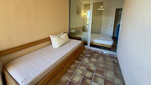 Habitació petita amb un llit individual, una porta corredissa de vidre i un sòl de rajola.