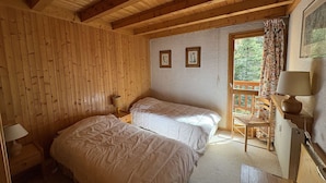 A wooden-paneled bedroom with two beds, a nightstand, a chair, and a window with a view of greenery. - Spacious apartment with parking - 6 guests (Méribel)