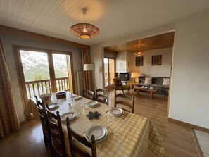 A dining area with a table set for four, wooden chairs, a checkered tablecloth, and a view of a mountainous landscape through large windows. - Spacious apartment with parking - 6 guests (Méribel)