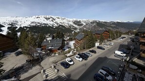 A mountain resort with snow-covered peaks, a parking lot, and wooden buildings. - Spacious apartment with parking - 6 guests (Méribel)