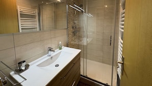 A modern bathroom with a glass-enclosed shower, a white sink, and a large mirror. - Spacious apartment with parking - 6 guests (Méribel)