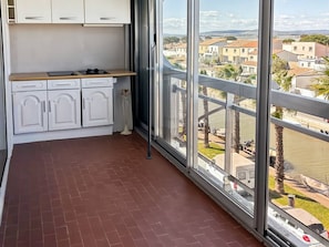 Ein Balkon mit Blick auf einen Fluss und Gebäude, eine Küche mit weißen Schränken und ein Fliesenboden.