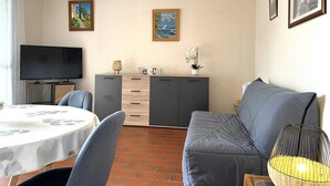 Un soggiorno con divano, televisore, tavolo da pranzo con sedie, credenza e due quadri appesi al muro.
