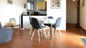 Zona pranzo con tavolo e sedie, cucina sullo sfondo e una porta che dà su un'altra stanza.