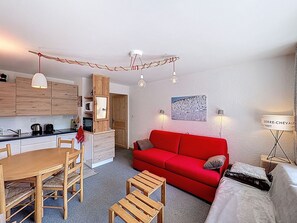 Ein kompakter Wohnbereich mit Essbereich, einem roten Sofa, einem kleinen Tisch und einer Küchenzeile.