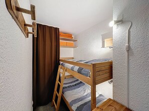En våningssäng med en stege, en gardin och en hylla med hopvikta filtar.