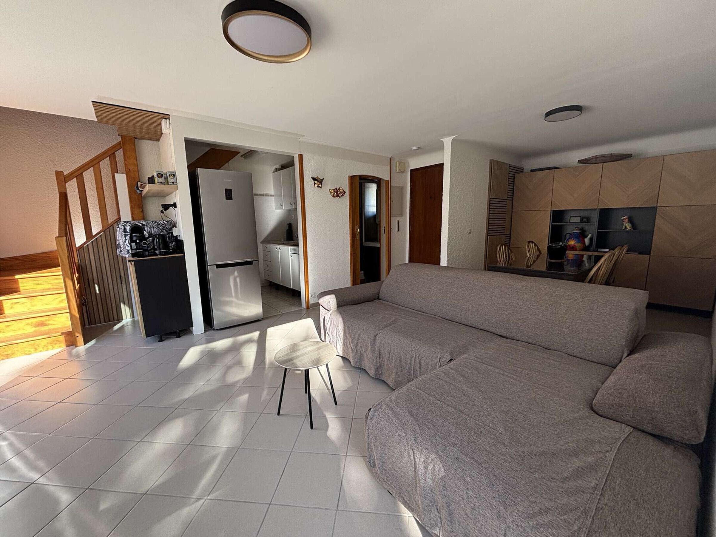 A living room with a sofa, a dining table with chairs, a kitchen area, and a staircase.