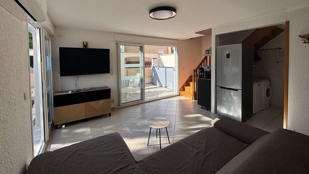 Un appartement moderne comprenant un salon, une cuisine, un téléviseur et une porte-fenêtre coulissante donnant sur un balcon.
