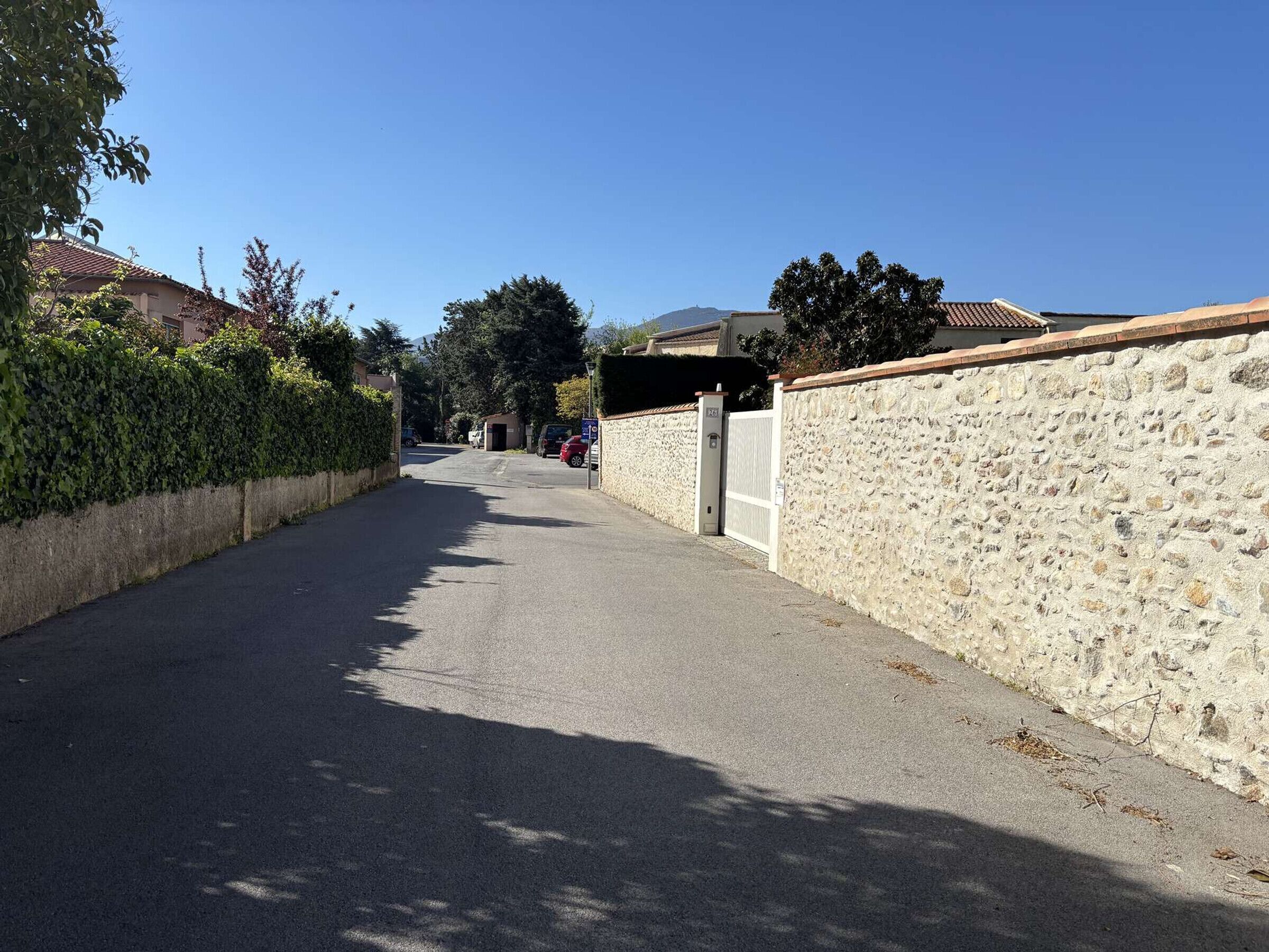 Une rue résidentielle bordée d’un côté par un mur de pierre et de l’autre par une haie.