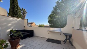 Une terrasse sur le toit avec un canapé noir, une petite table, une plante en pot et une étagère en métal.