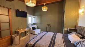 Une chambre à coucher avec un lit, des tables de chevet, une télévision, une fenêtre et un luminaire suspendu.