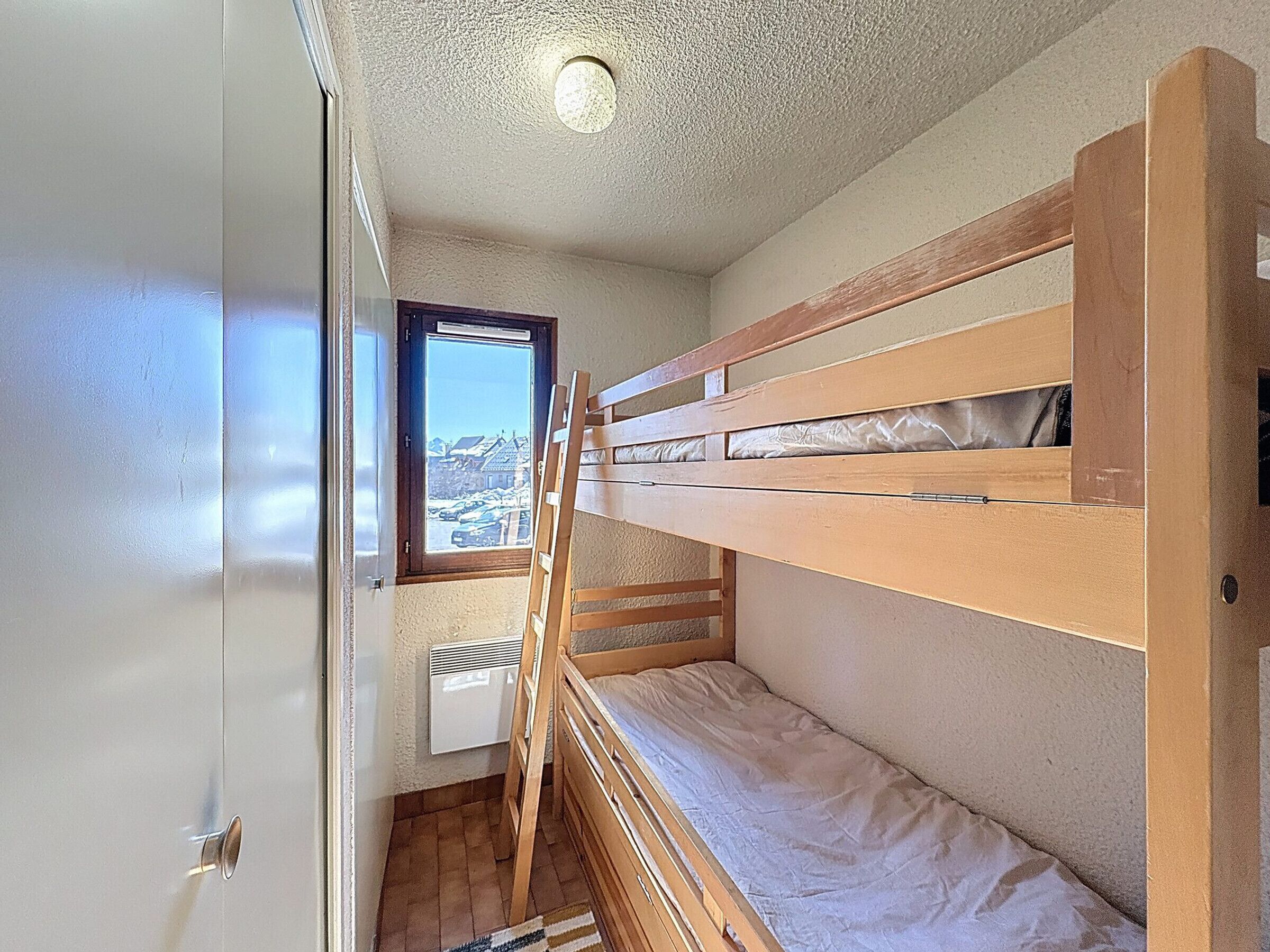 Une petite pièce, de taille modeste, comprenant un lit superposé, une fenêtre donnant sur un paysage agréable, un radiateur et une porte.