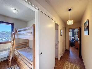Ein Zimmer mit Etagenbett, einer Leiter, einem Fenster mit Blick und einem Flur, der in ein weiteres Zimmer führt, sowie einer Pendelleuchte.