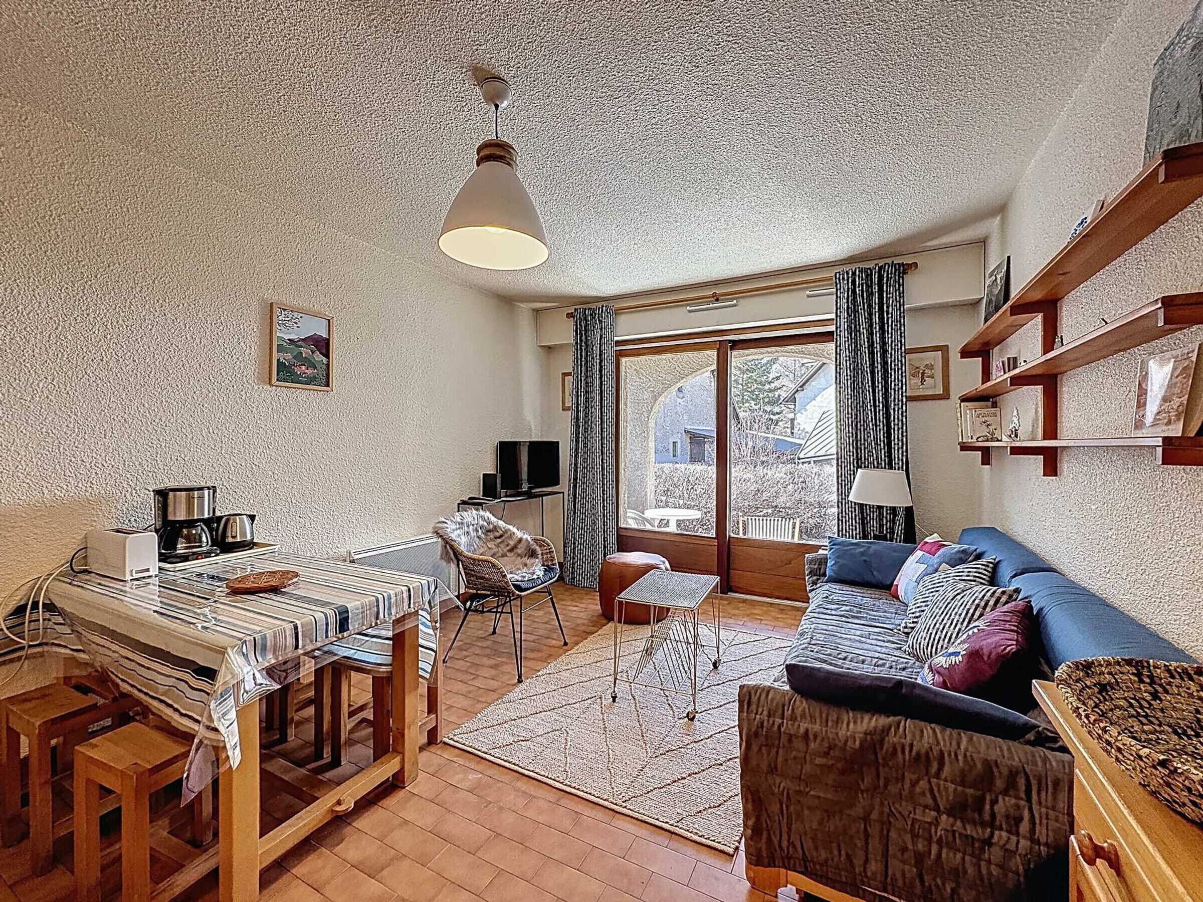 A cozy living room with a dining area, a television, and a large window with curtains.