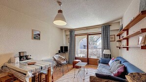A cozy living room with a dining area, a television, and a large window with curtains. - Central studio with terrace - 4 guests (Le Monêtier-les-Bains)