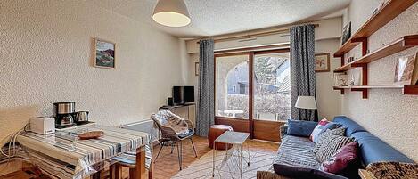 A cozy living room with a dining area, a television, and a large window with curtains.