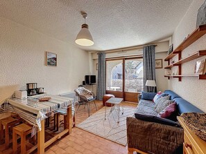 Ein gemütliches Wohnzimmer mit Essbereich, Fernseher und einem großen Fenster mit Vorhängen.