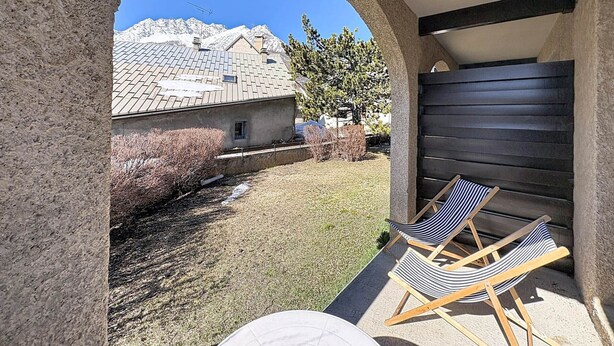A covered outdoor seating area with two striped lounge chairs, a stone archway, and a view of a mountain. - Central studio with terrace - 4 guests (Le Monêtier-les-Bains)