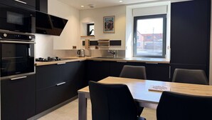 Una cocina moderna con armarios negros, horno integrado, microondas y un comedor con mesa y sillas.