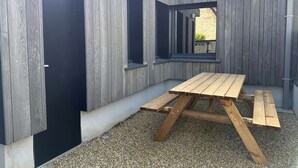 Una terraza de madera con una mesa de picnic, una puerta y ventanas.