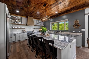 A modern kitchen with a large island, wooden ceiling, and a view of trees through a window. - Now Open! Be the first to stay in The Grand View! (Sevierville)