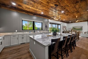 A modern kitchen with a large island, grey cabinets, wooden ceiling, and large windows. - Now Open! Be the first to stay in The Grand View! (Sevierville)