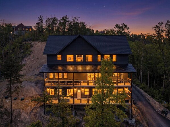 A multi-story house with a large balcony, surrounded by trees and a dirt path. - Now Open! Be the first to stay in The Grand View! (Sevierville)