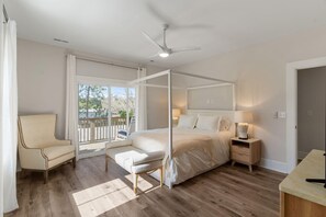 A bedroom with a four-poster bed, a chair, a bedside table, and a view of the outdoors. - Driftwood at Seagate - We love Doggies (Wilmington)