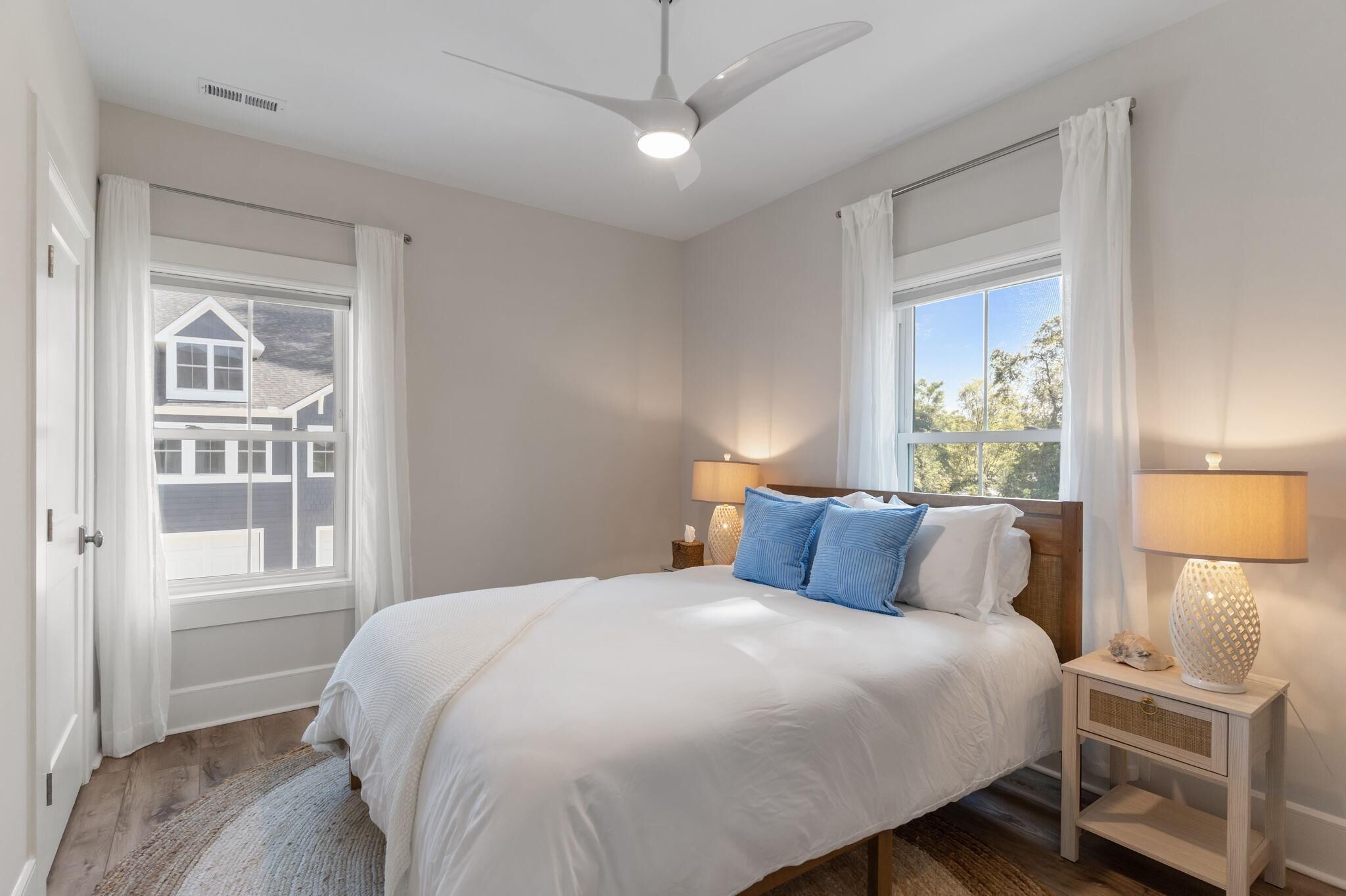 A bedroom with a bed, two bedside tables, a ceiling fan, and two windows with curtains.