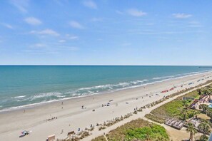 Ein Strand mit weitem Sandstreifen, einem Pier in der Ferne und wolkenlosem Himmel.