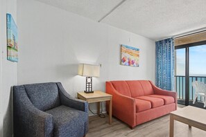 A room with a grey armchair, a red sofa, a small wooden table with a lamp, and a painting on the wall. - Oceanfront 1BR + Beach Access + Dog Friendly (Myrtle Beach)
