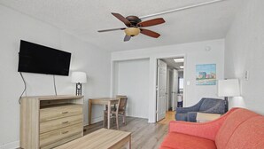 Una sala de estar moderna con un escritorio de madera, un sofá, un televisor y un ventilador de techo.