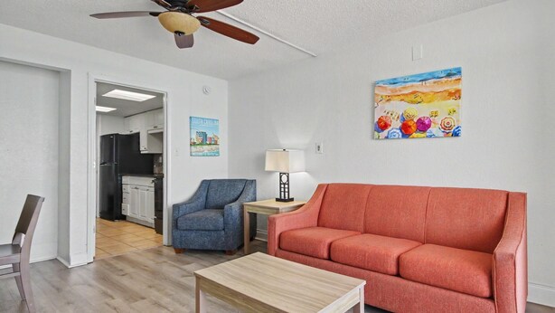 A living room with a wooden coffee table, a red sofa, a blue armchair, a lamp, and a painting on the wall. - Oceanfront 1BR + Beach Access + Dog Friendly (Myrtle Beach)
