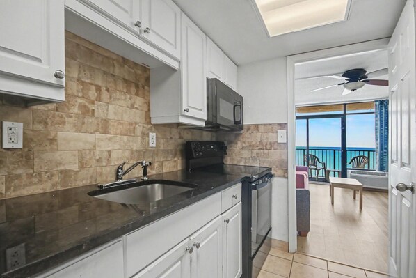 Una cocina moderna con microondas incorporado, lavavajillas y pileta. Hay un balcón con vista al mar.