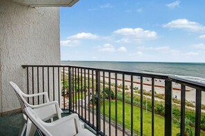 A balcony with white plastic chairs, a view of the beach, and a clear sky. - Ocean 1BR + Beach Access + Dog Friendly (Myrtle Beach)
