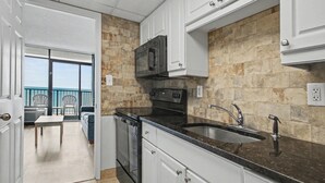 Cocina con gabinetes blancos, encimera negra y salpicadero de piedra.