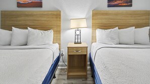 Habitación de hotel con dos camas, una mesita de noche con lámpara y dos cuadros en la pared.