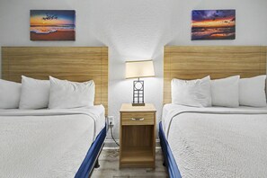 Une chambre d’hôtel avec deux lits, une table de chevet avec une lampe et deux tableaux au mur.