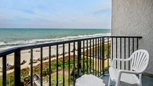 Un balcón con vista a la playa y al océano, sillas de plástico blanco y una barandilla.