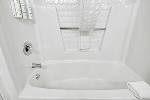 Une baignoire blanche, avec un rideau de douche, un robinet et une serviette posée sur le bord.
