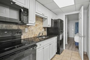 Una cucina con mobili bianchi, un piano cottura nero, un forno a microonde e un frigorifero.