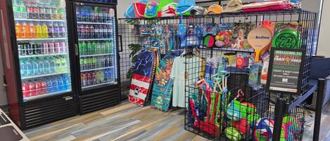 Zona de bar con neveras de Coca-Cola y Pepsi, una variedad de aperitivos y una exhibición de juguetes y accesorios de playa de colores.