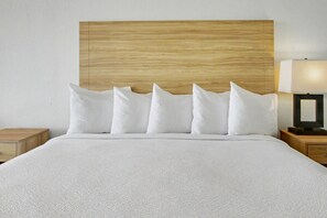 Una cama con cabecera de madera, ropa de cama blanca y una mesita de noche con una lámpara.