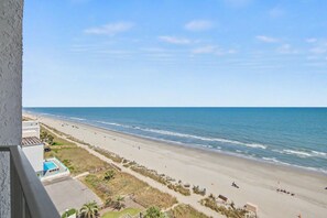 A beach view from a balcony with a pool, beach umbrellas, and a clear sky. - Oceanfront King Room + Beach Access + Dog Friendly (Myrtle Beach)