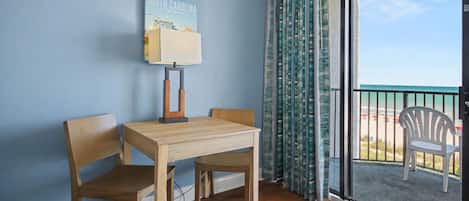 A room with a table and two chairs, a view of the beach, and a sign on the wall.