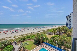 A beach view with a pool, palm trees, and a hotel building. - Oceanfront King Room + Beach Access + Dog Friendly (Myrtle Beach)