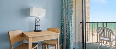 Una habitación con una mesa y sillas de madera, una lámpara de pie y vistas al mar a través de un ventanal.