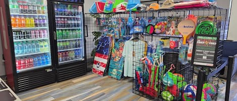 A snack bar area with a Coca-Cola and Pepsi refrigerator, a variety of snacks, and a display of colorful beach toys and accessories.